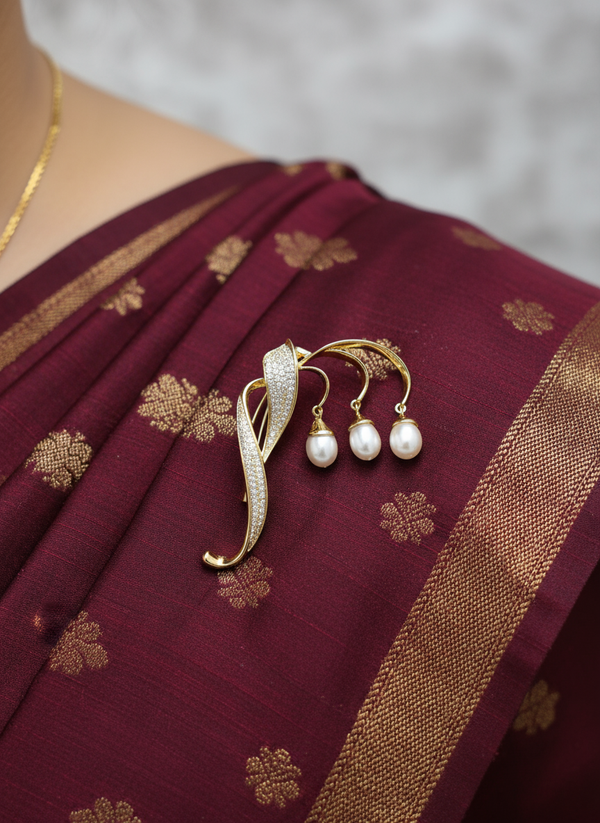 Close-up of unisex gold brooch with three pearl drops styled as a saree pin on maroon silk saree
