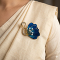 Close-up of blue swan brooch with thread and fabric wing, pearl accents and crystal-studded body pinned on a cream saree.