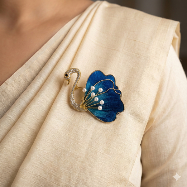 Close-up of blue swan brooch with thread and fabric wing, pearl accents and crystal-studded body pinned on a cream saree.