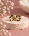 Dewlight Spark Studs with sculpted gold-tone borders and clear pear-shaped stones on an ivory pedestal