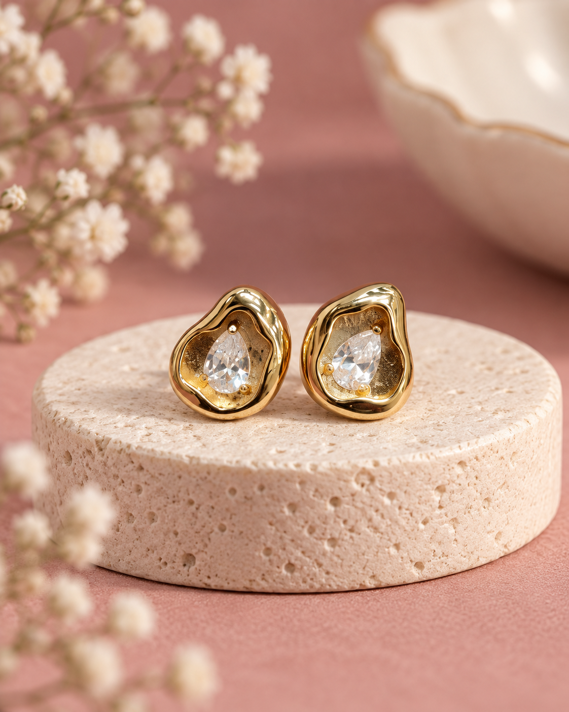 Dewlight Spark Studs with sculpted gold-tone borders and clear pear-shaped stones on an ivory pedestal
