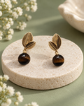 Dusk & Dew Drops earrings with gold-tone leaves and dark brown bead drops on an ivory pedestal