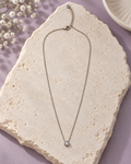 Moonlit Dot Necklace with a fine silver-tone chain and round clear stone pendant on ivory stone