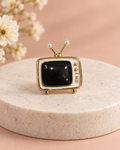 Retro Rewind Brooch with cream, black and gold-tone TV details on an ivory pedestal and peach background