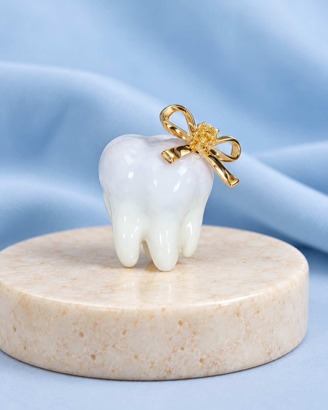 The Smile Signature Brooch: glossy white tooth with a gold-tone bow on a soft powder-blue background