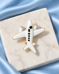 Wanderwing Brooch: glossy white airplane with black windows and gold-tone edging on sky-blue satin and ivory stone